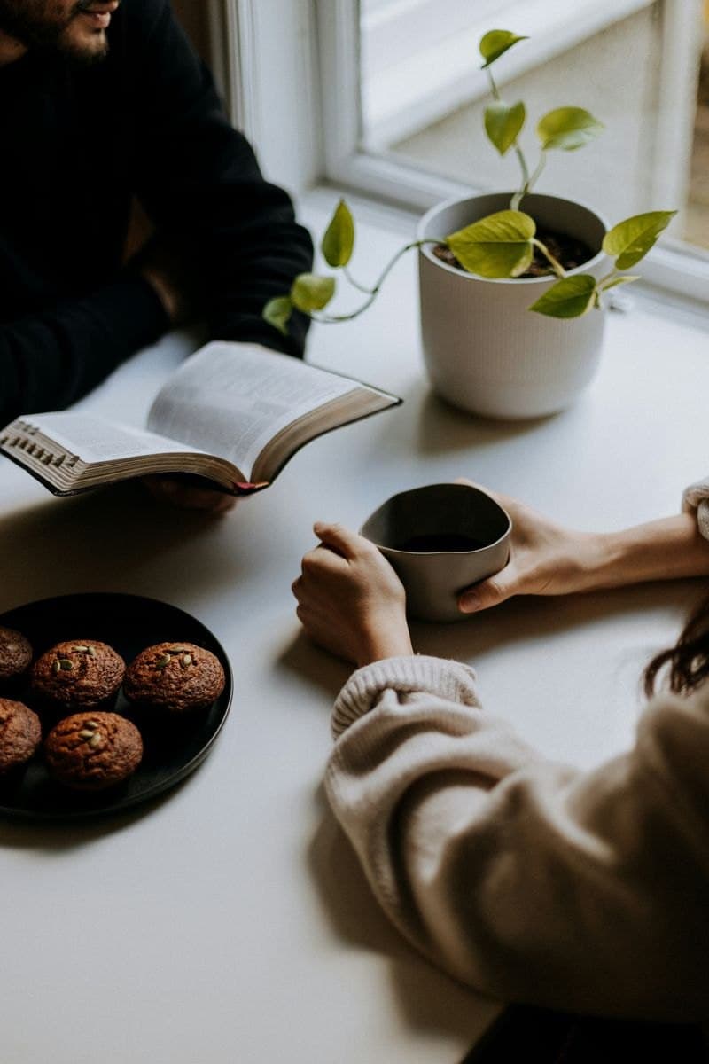 To personer i samtale ved et bord med kaffe og en plante